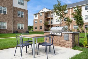 A table with two chairs is in front of a brick wall with a grill on top.